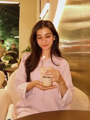 Ateeqa in a blush outfit with a latte at a café